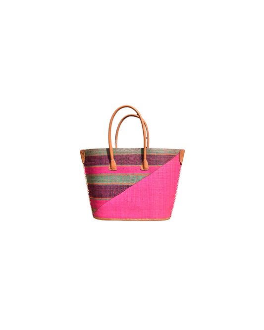 “Handmade raffia handbag from Madagascar with fuchsia pink base and green and plum striped design, featuring leather handles and reinforced corners.”