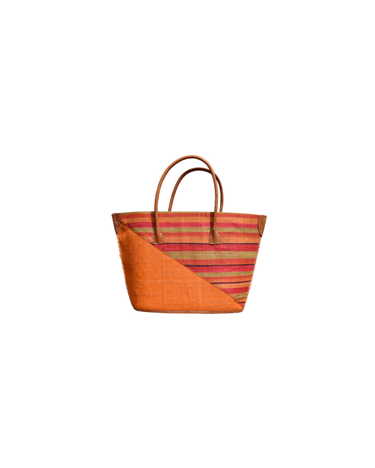 “Handmade raffia handbag from Madagascar with bright amber-orange base and red, plum, and green striped design, finished with leather handles and reinforced corners.”